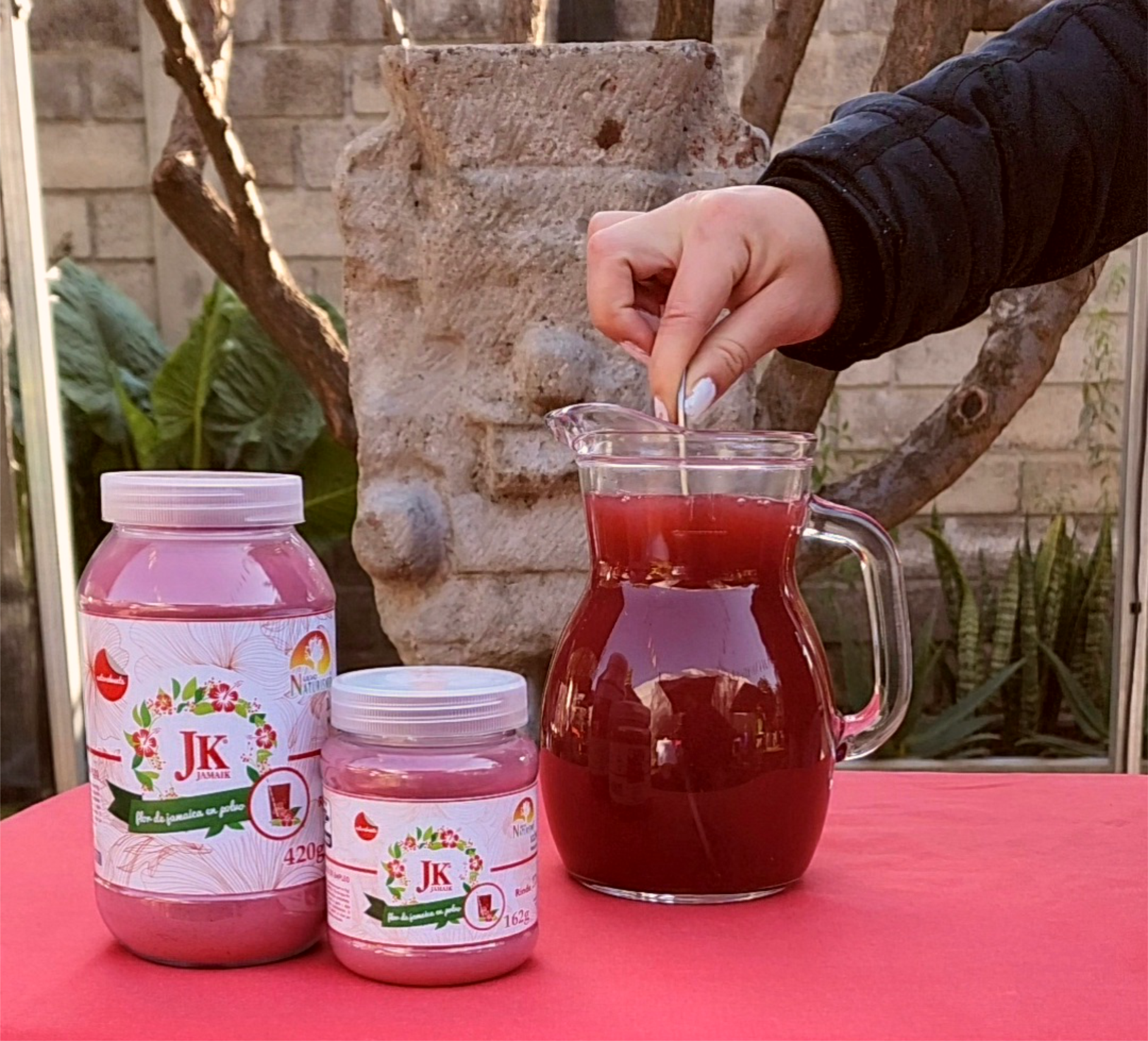 Dos frascos de JK JAMAIK junto a una jarra de agua de jamaica.